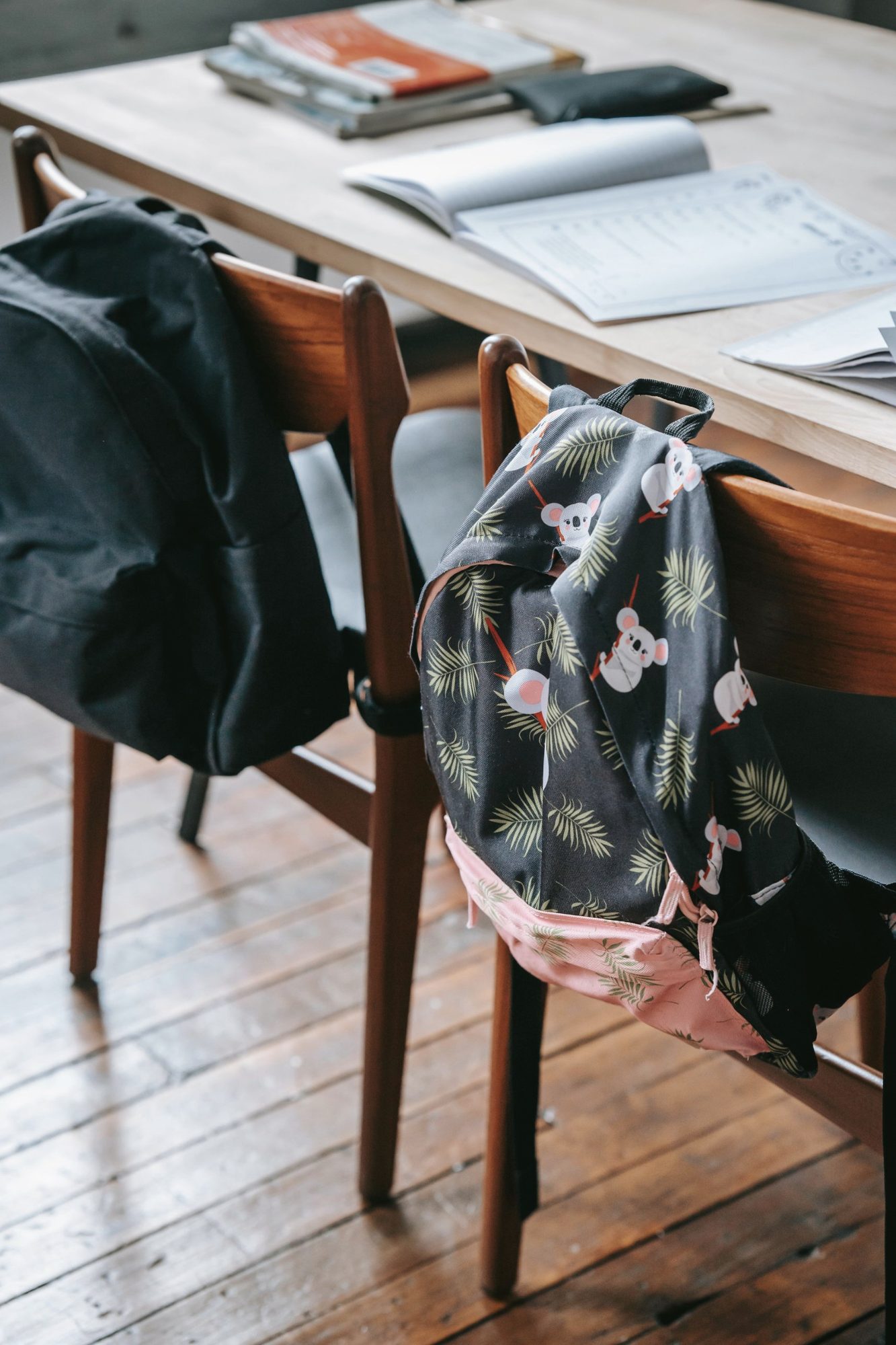 Two school backpacks hung on chairs at a classroom table with open workbooks