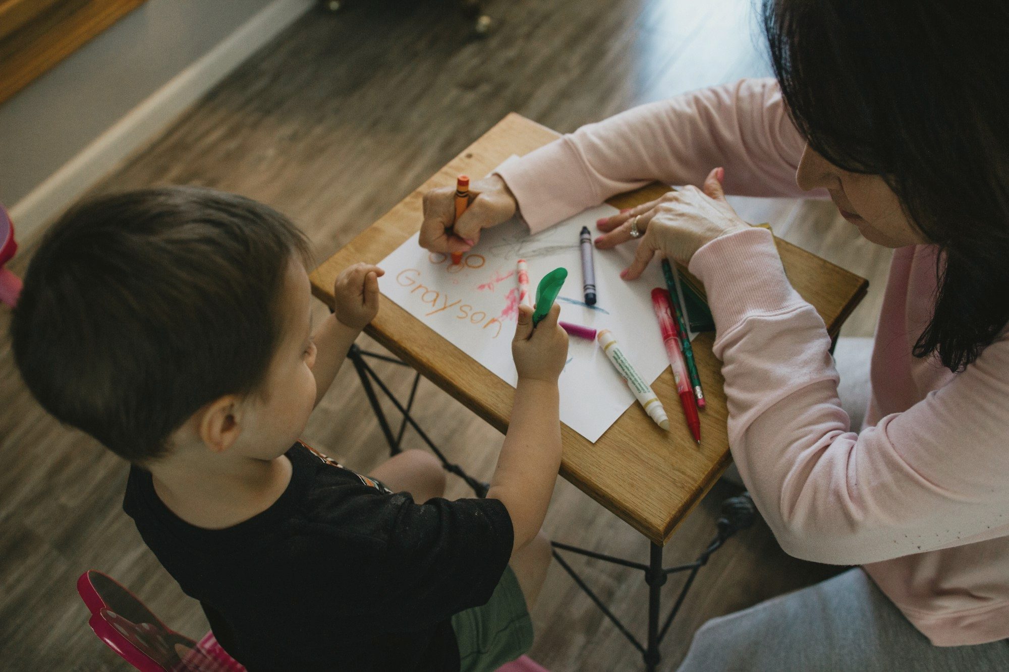 An adult and a young child colouring side by side at a small table