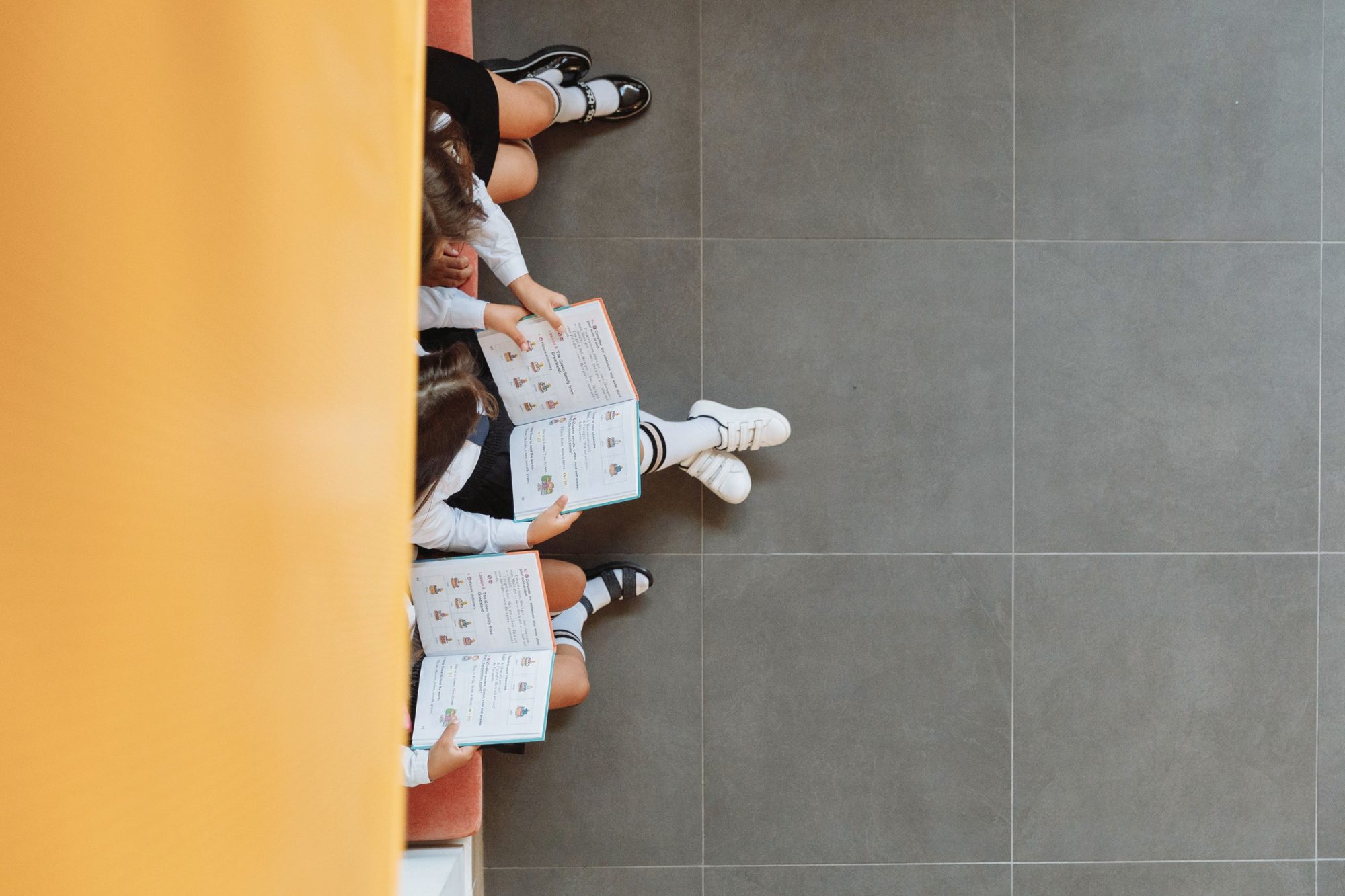 Looking down on three students in uniform reading the same workbook side by side